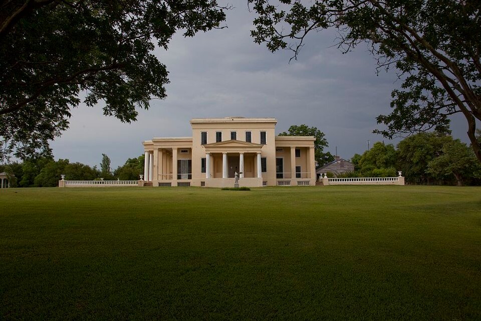 Front portico of Gaineswood with a statue, seen across the lawn under a cloudy sky