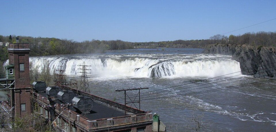 Cohoes Falls en primavera, con el río cayendo por el ancho borde rocoso junto a un edificio de una central eléctrica