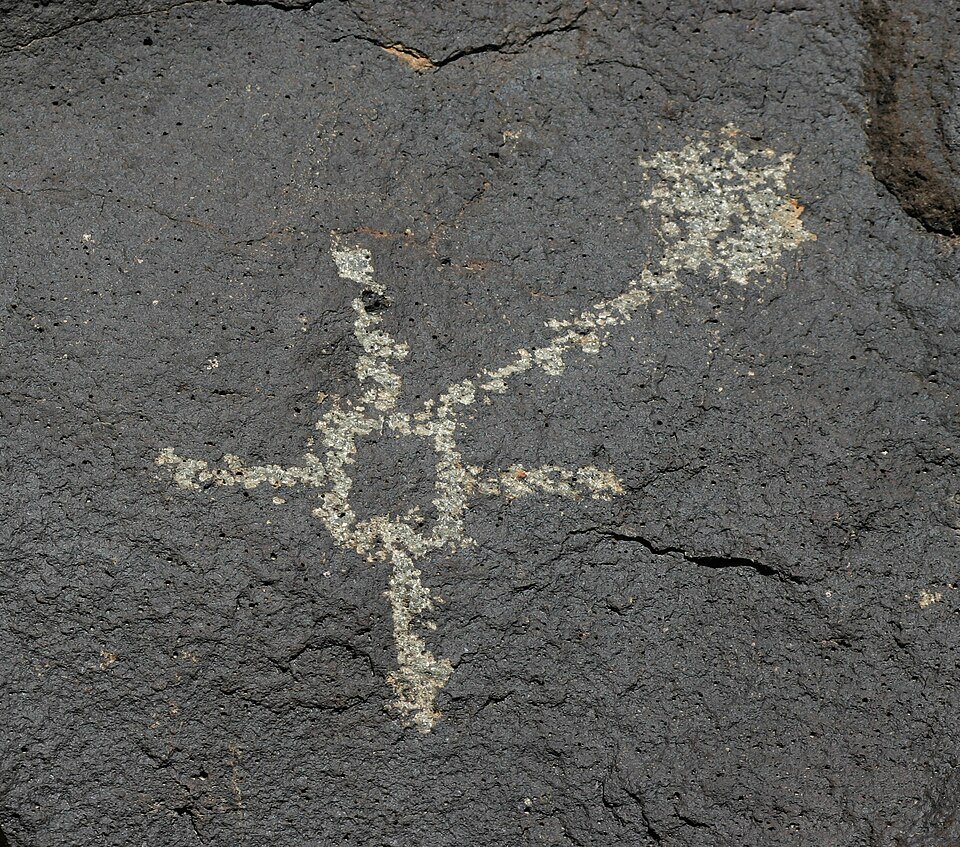Un petroglifo de una figura con extremidades extendidas grabado en basalto oscuro