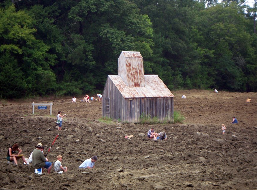 Visitors digging in the plowed field at Crater of Diamonds State Park, with a small weathered wooden building in the middle