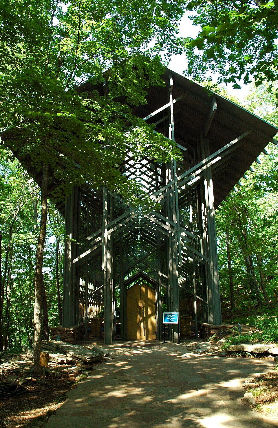 Front of Thorncrown Chapel, a tall glass and wood building among trees, with a flagstone path leading to the door