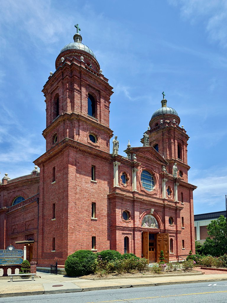 Fachada da basílica: tijolo vermelho, duas torres com cúpulas e estátuas sobre a cornija