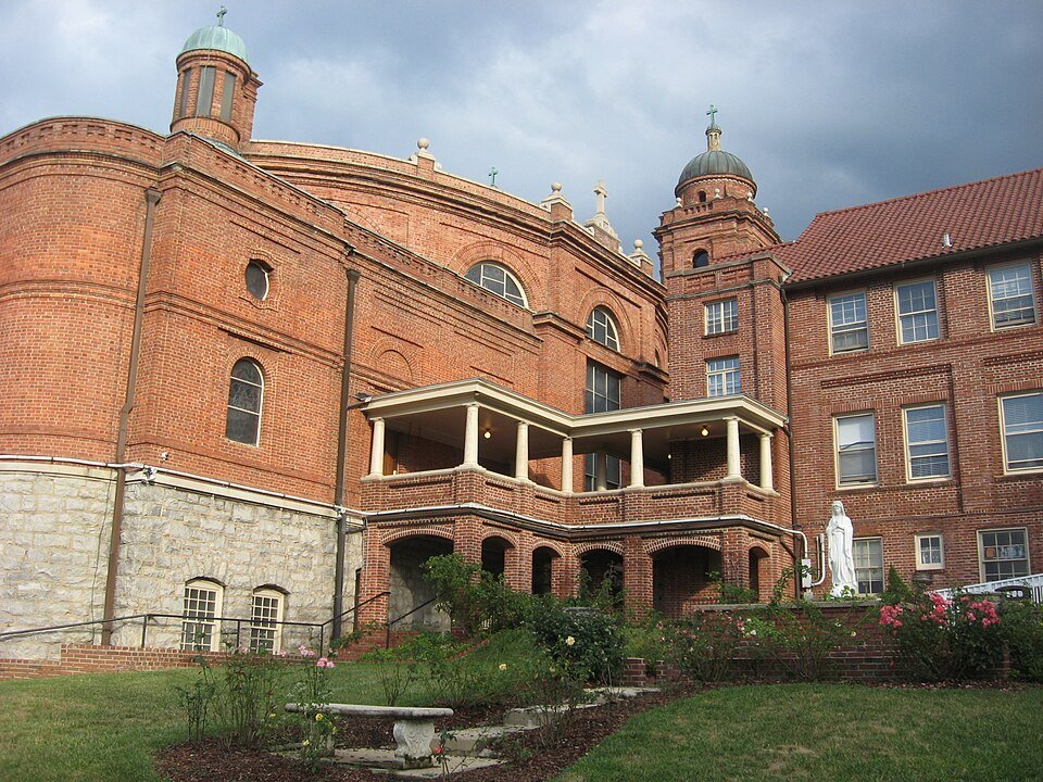 Os fundos de tijolo da basílica, com uma sacada coberta e uma estátua branca da Virgem Maria