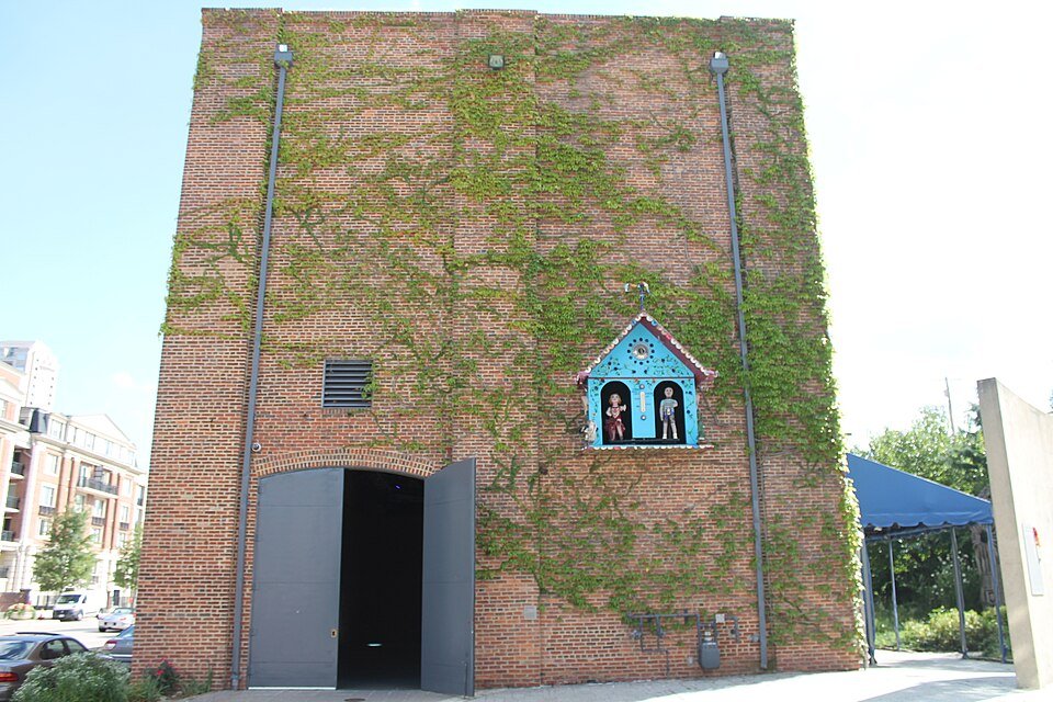 Tall brick wall covered in ivy at the museum, with a small blue house holding two figures