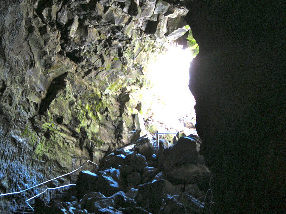 The cave entrance seen from below, with a pile of fallen rock, a handrail and daylight coming in