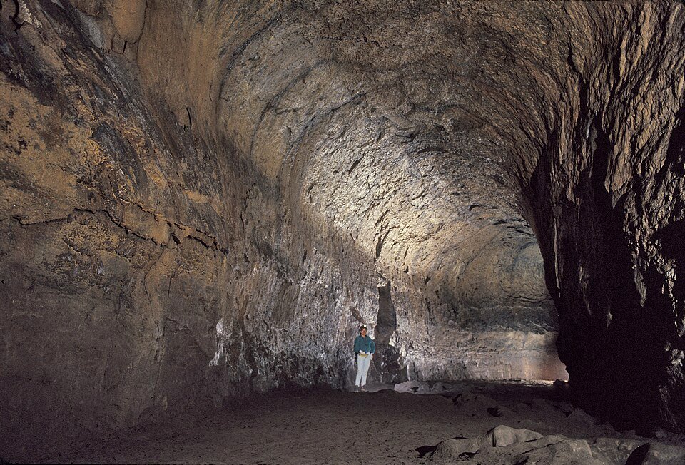 A large, high-ceilinged lava tube chamber with a small visitor standing at the center