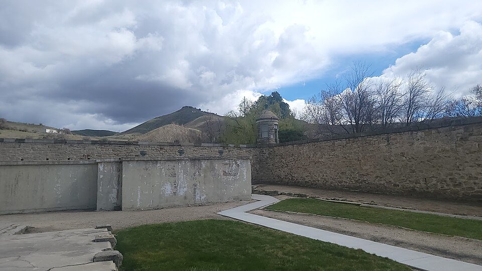 Un patio amurallado del Old Idaho Penitentiary, con una torre de vigilancia de piedra y colinas secas al fondo