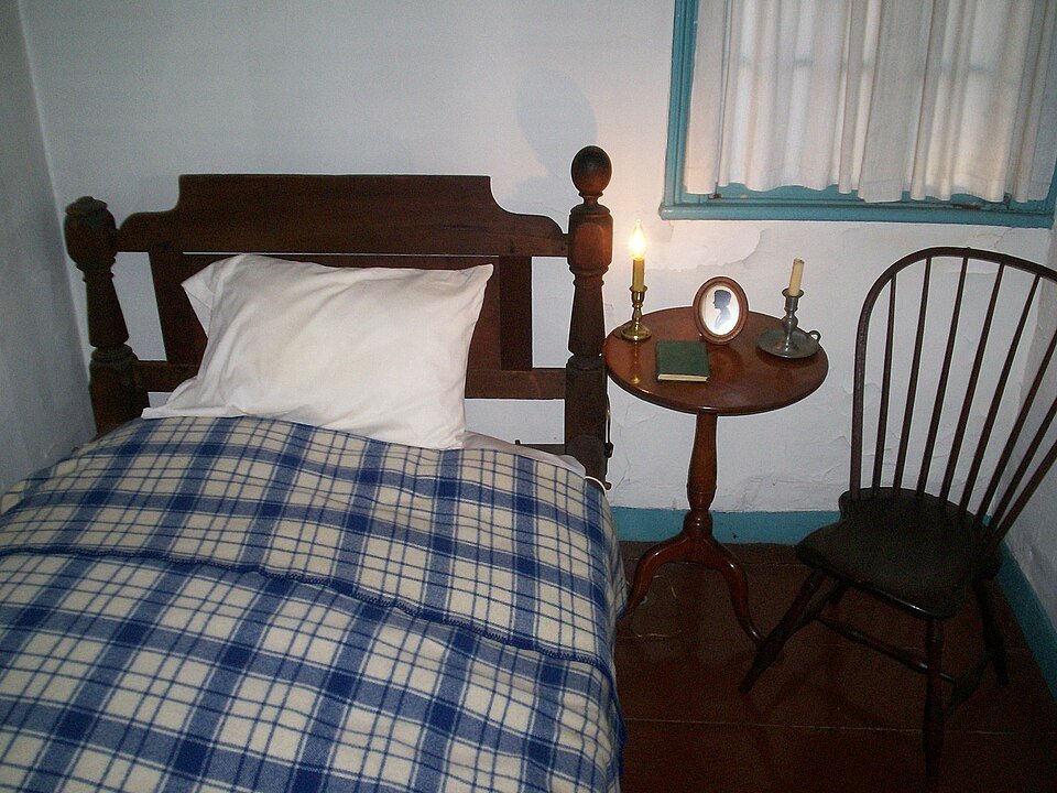 A bedroom furnished in period style in the Poe Cottage, labeled Virginia Poe’s bedroom