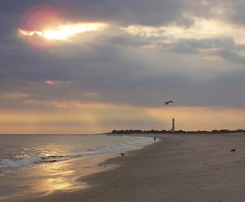 A beach at Cape May Point at sunset, with the lighthouse far off along the shore