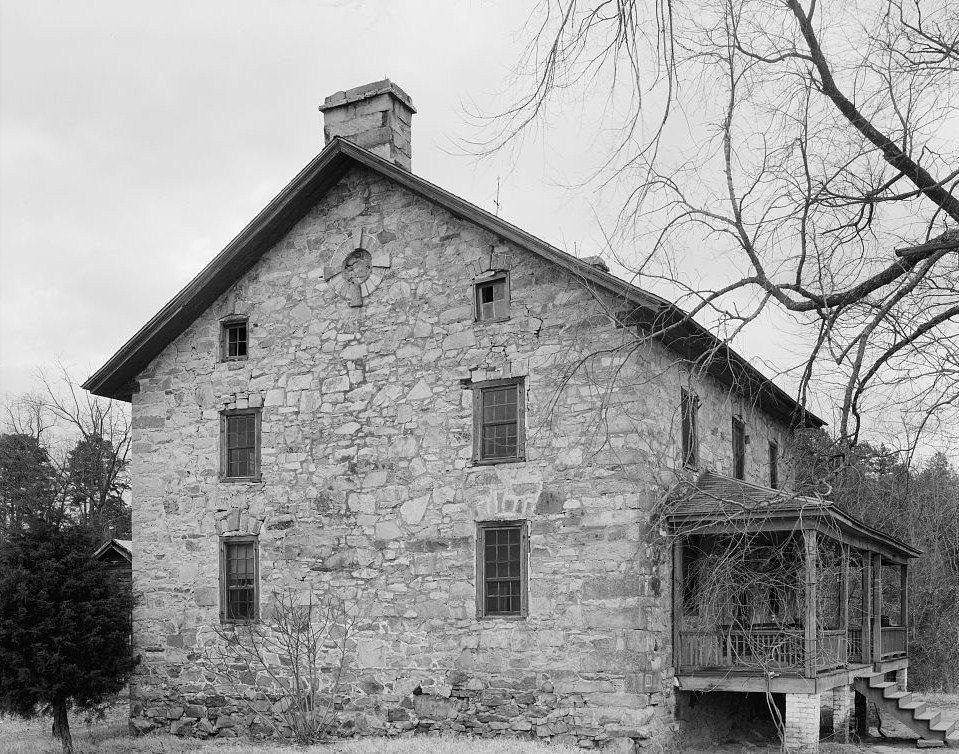 Historic black-and-white photograph of the stone house, showing its stonework and a side porch