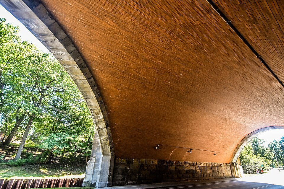 A parte inferior, revestida de tijolo, de uma ponte de pedra em arco no Rockefeller Park, com árvores ao fundo