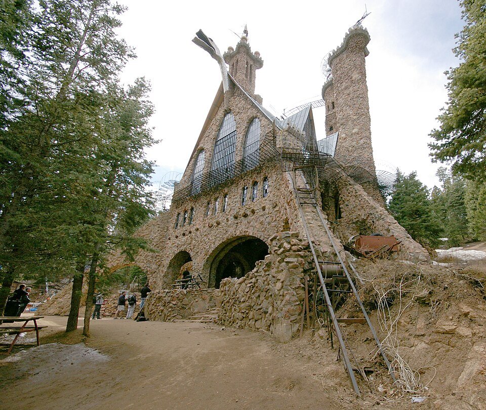 Bishop Castle seen from the front: a stone castle with towers, a metal stairway and a few visitors near its arches
