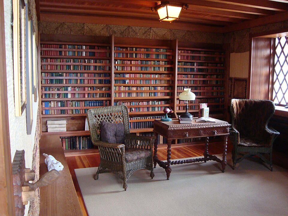 Library inside Gillette Castle with dark woodwork, bookshelves and wicker chairs