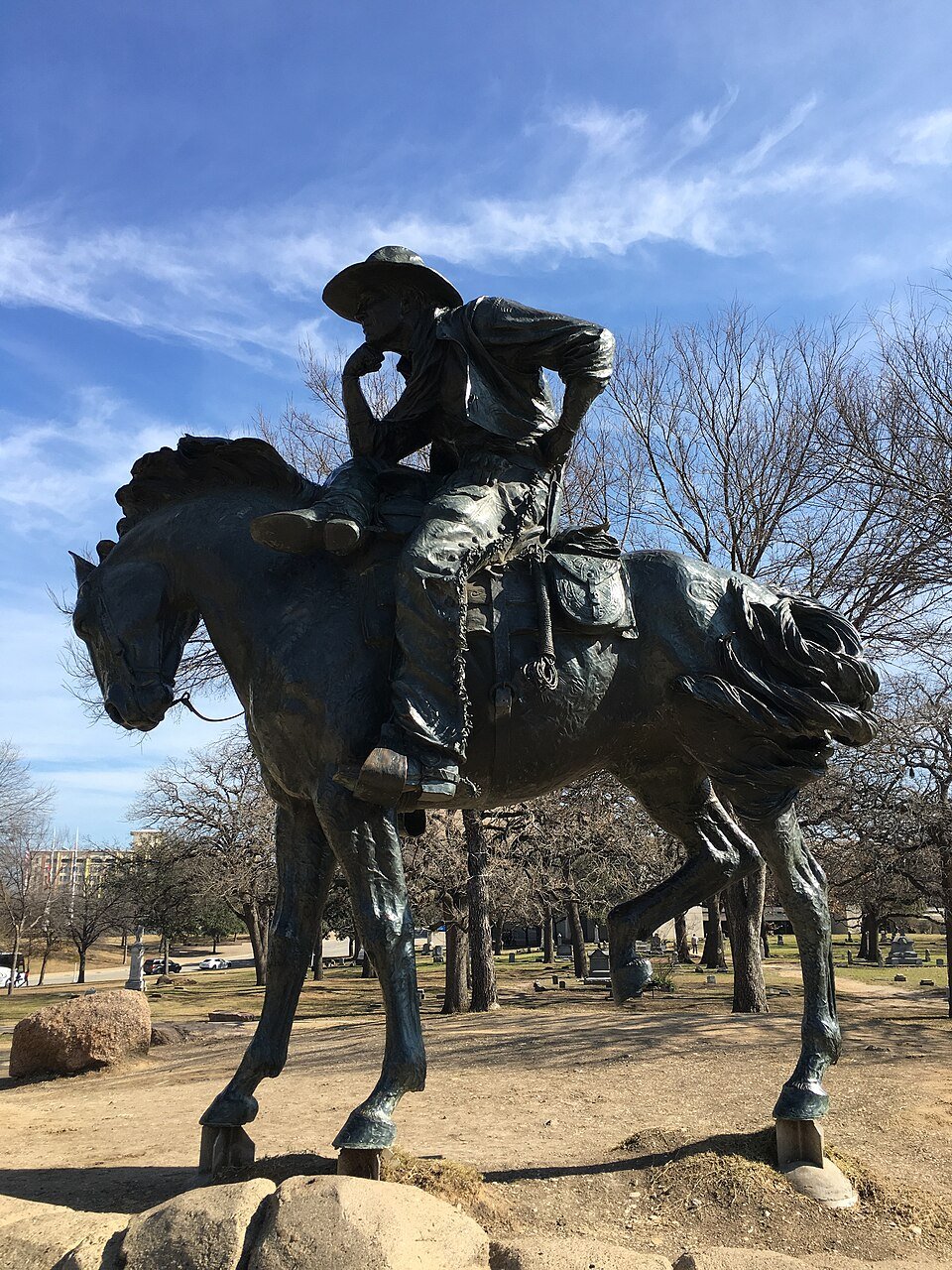Cavaleiro de bronze a cavalo, com o queixo apoiado na mão, contra um céu azul e árvores sem folhas