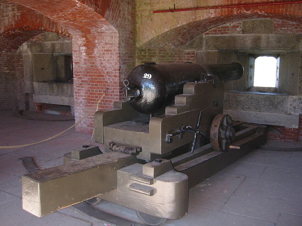 A black cannon on a wooden carriage inside a brick casemate at Fort Delaware