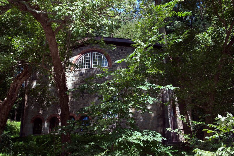 A restored stone mill at Hagley seen through trees, with a large arched window