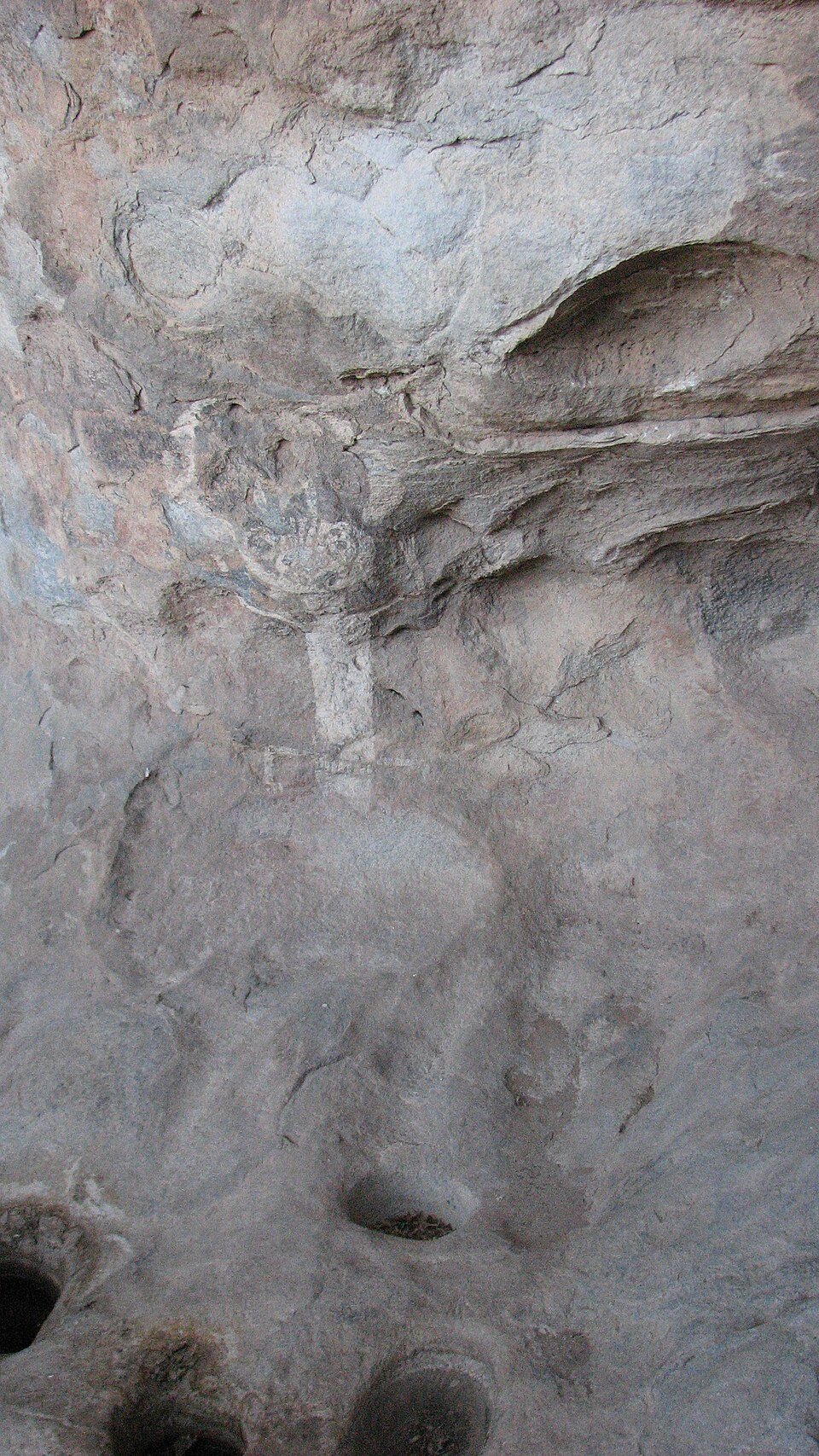 A rock wall with a faint painted figure above worn grinding holes known as metates, near the White Horned Dancer pictograph