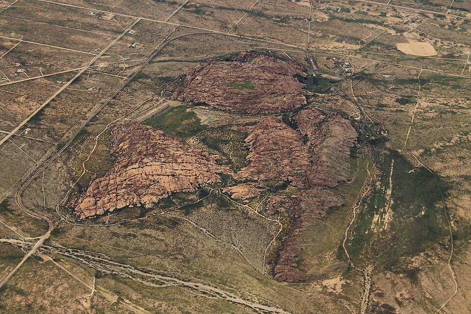 Aerial view of the three rock mountains of Hueco Tanks rising from the desert floor, with dirt tracks around them