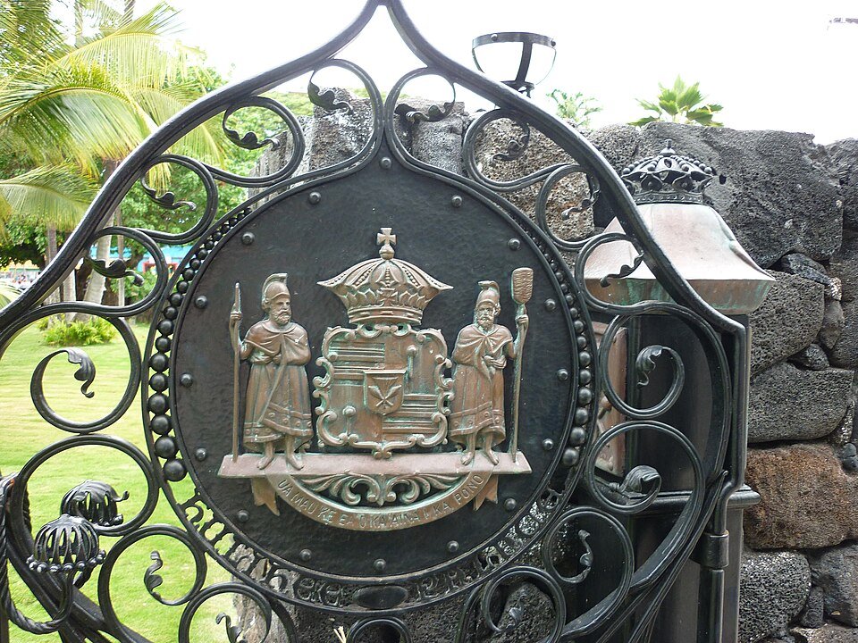 Reja de hierro forjado con el escudo real, dentro de un muro de roca de lava, en la entrada del terreno