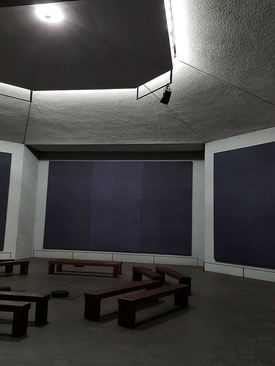 Interior of the Rothko Chapel, with dark paintings on the wall and wooden benches