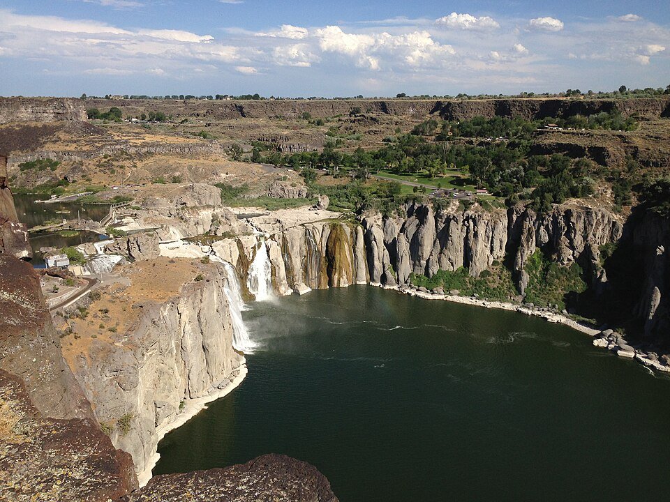 Shoshone Falls in Idaho seen from the northwest: the falls at the far end of a dark green pool, with basalt cliffs and a park beyond