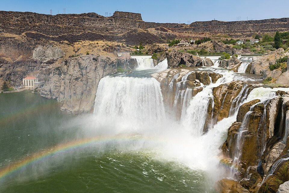 Shoshone Falls on the Snake River, with a rainbow over the green pool below and a small building at the foot of the canyon wall