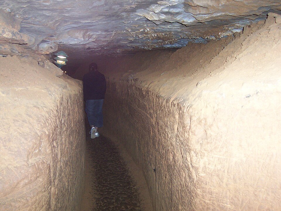 Narrow passage with clay-colored walls and a lamp inside Wyandotte Cave