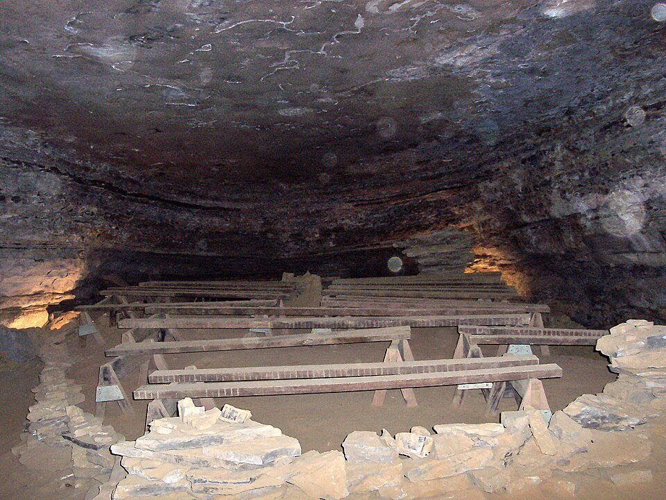 Wooden trestles resting on the floor of a cave chamber behind a low wall of stacked stone