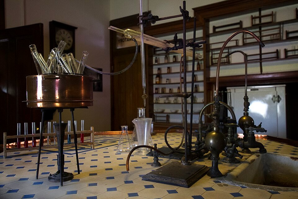 Laboratorio de química con una olla de cobre, material de vidrio y grifos de latón sobre una mesada de azulejos
