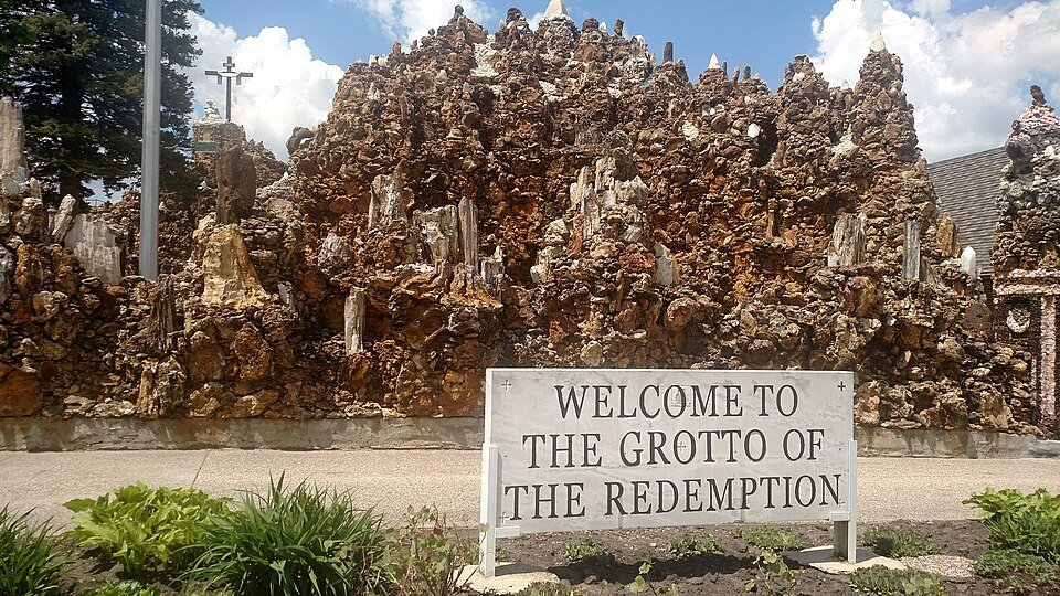 El muro rugoso de rocas y minerales detrás del cartel de bienvenida de la Grotto of the Redemption