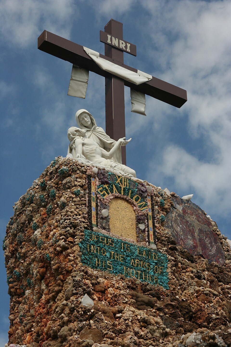 La estación 13 de la Grotto of the Redemption: una estatua de la Piedad y una cruz sobre un muro de minerales