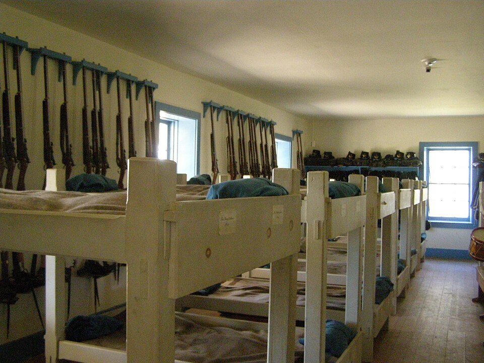 Inside a barracks at Fort Larned, with bunks and rifles on the wall