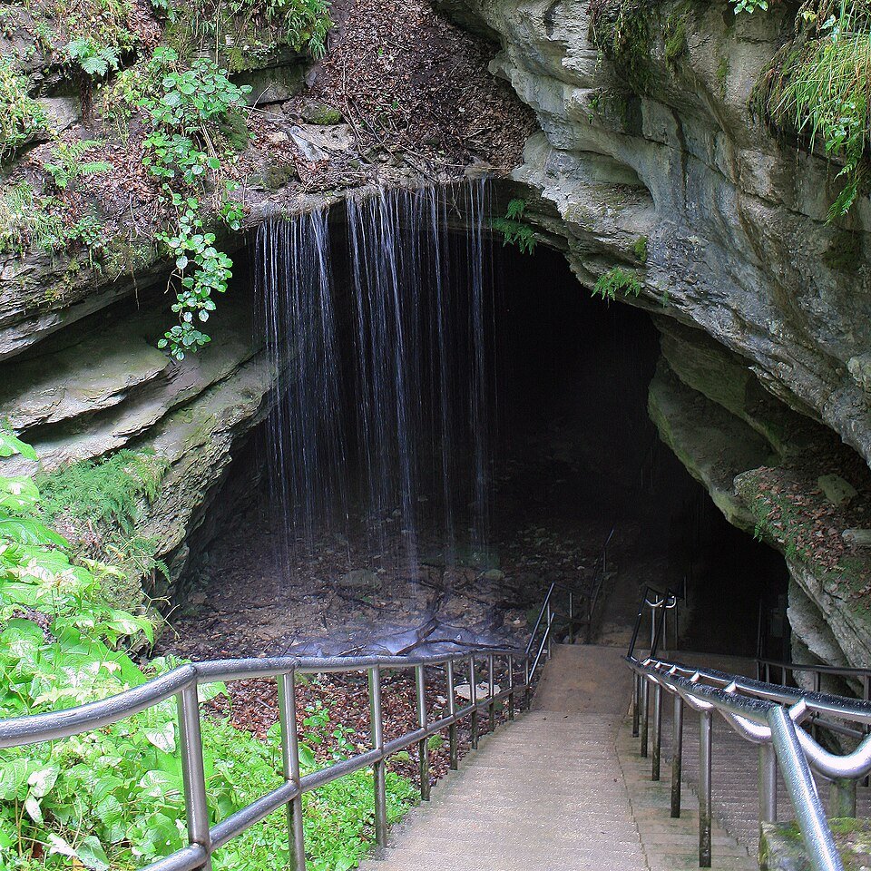 Historic entrance to Mammoth Cave: a stairway with handrails descends under a veil of falling water into a rock opening