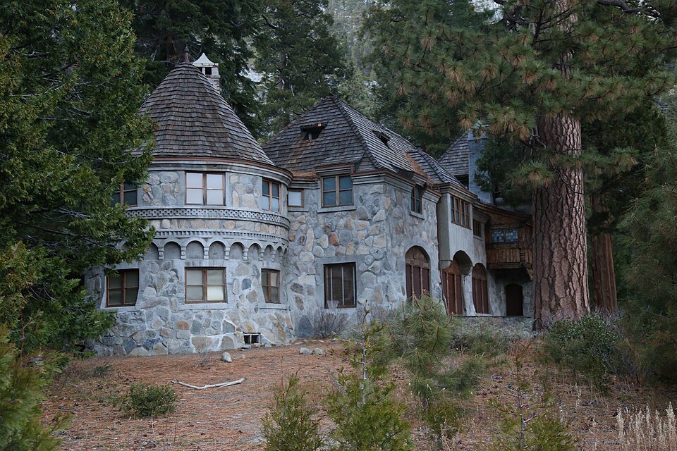 The round stone tower of Vikingsholm with its shingled conical roof, among pine trees