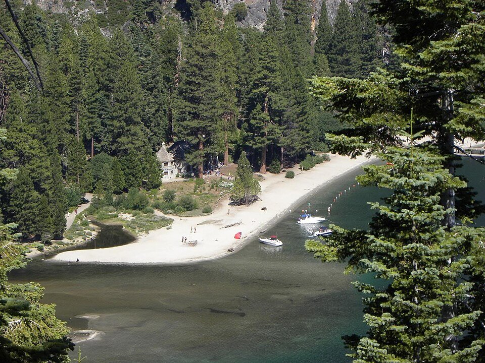 Vikingsholm among the trees behind a sandy beach on Emerald Bay, with boats anchored offshore