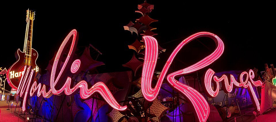 O letreiro do Moulin Rouge aceso em néon rosa à noite, com o letreiro de guitarra do Hard Rock Cafe à esquerda