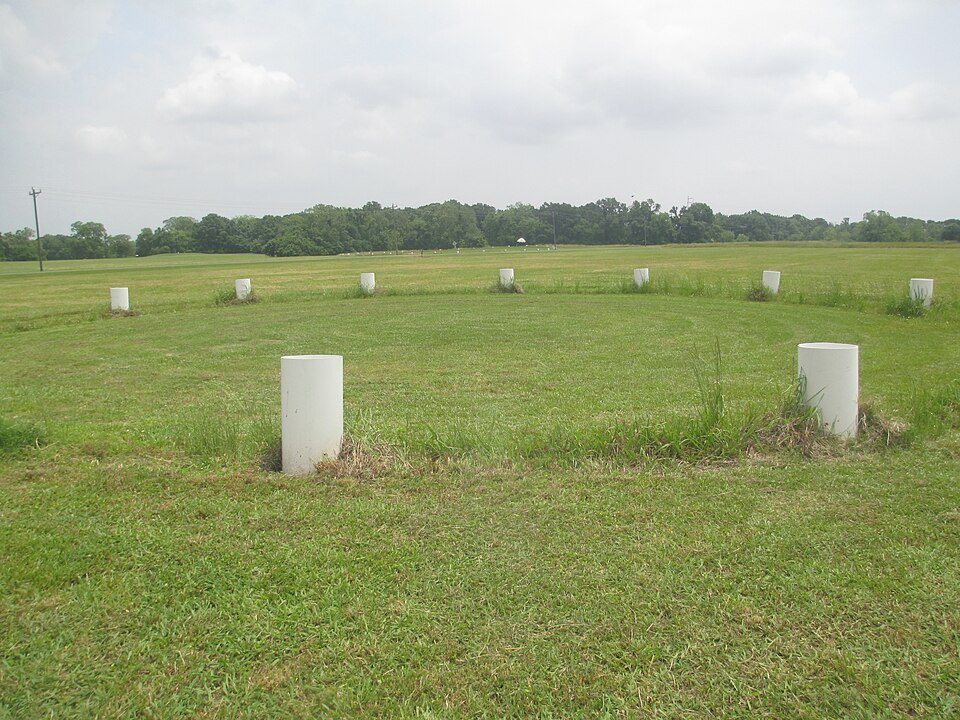White marker posts outlining a circle of wooden posts in the plaza