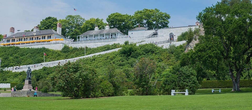 Fort Mackinac's white buildings and walls on the hillside above a lawn, with a statue at left