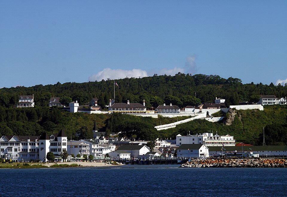 White walls and buildings of Fort Mackinac on the wooded bluff above the harbor of Mackinac Island