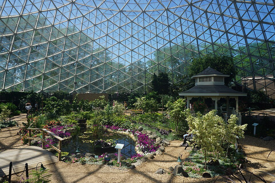 A garden with a pond, a small bridge and a gazebo under the glass of the Floral Show Dome during a summer show
