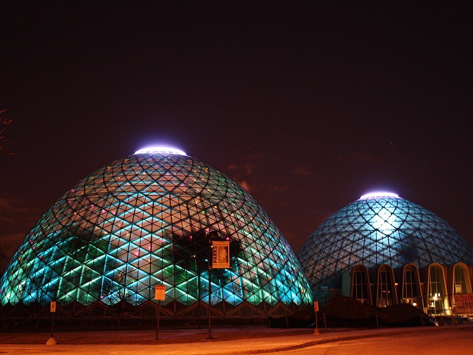 Two of the glass domes lit in blue and green at night, with the entrance building at right