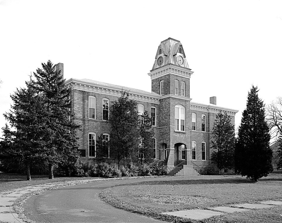 Un edificio de ladrillo con torre de reloj y altas ventanas en arco en Fort Snelling, en una fotografía antigua en blanco y negro