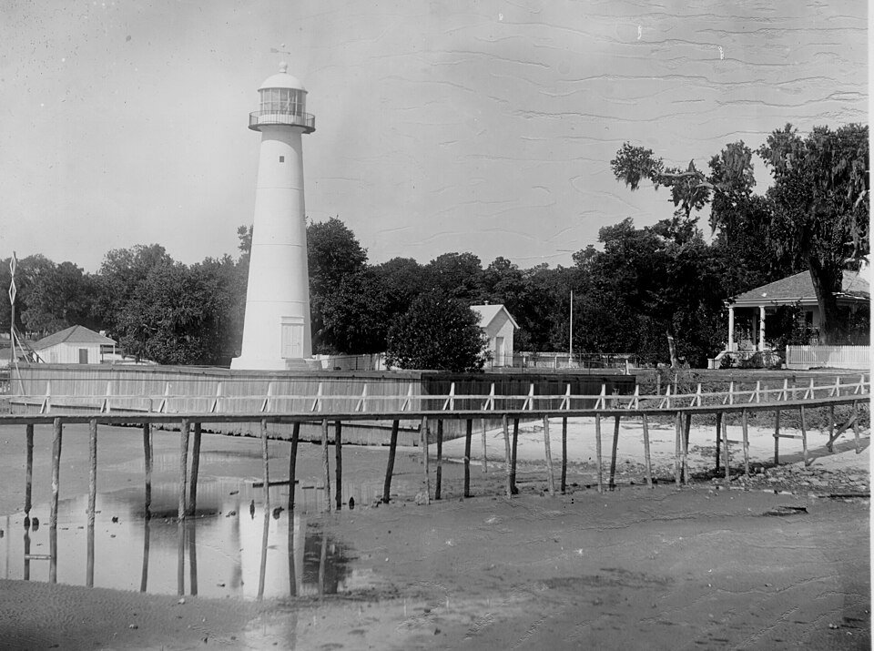 Foto histórica en blanco y negro del faro de Biloxi, con una pasarela de madera en primer plano