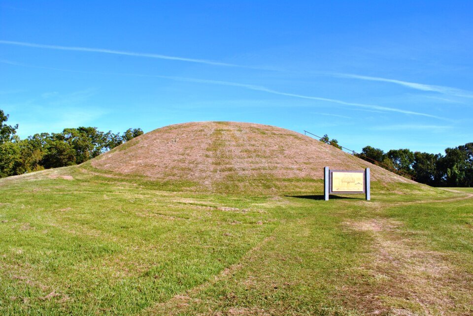 Grass-covered slope of Emerald Mound with an interpretive sign at its foot