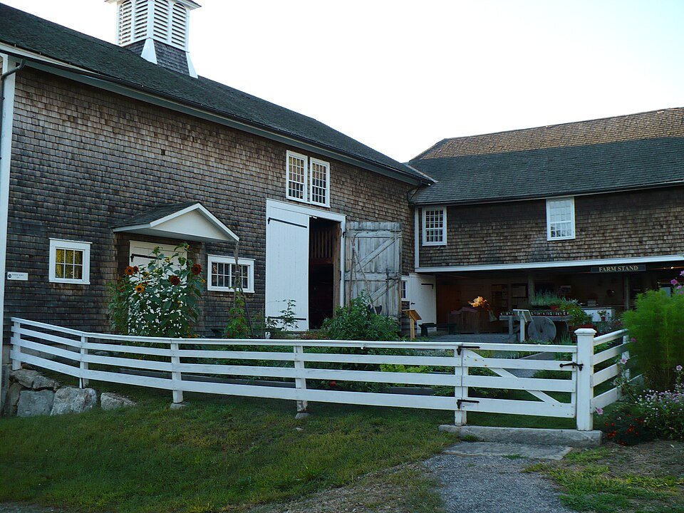 The Horse Barn at Canterbury Shaker Village, a shingled farm building beside a white fence and a farm stand