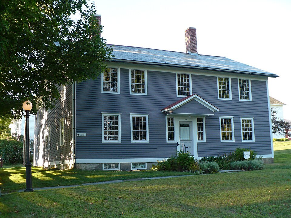 The Infirmary at Canterbury Shaker Village, a two-story gray-blue clapboard building with a small entry porch