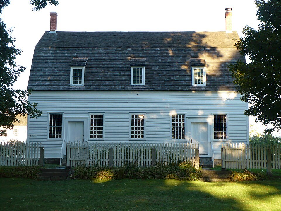 The Meetinghouse at Canterbury Shaker Village, a white clapboard building with a gambrel roof and a picket fence