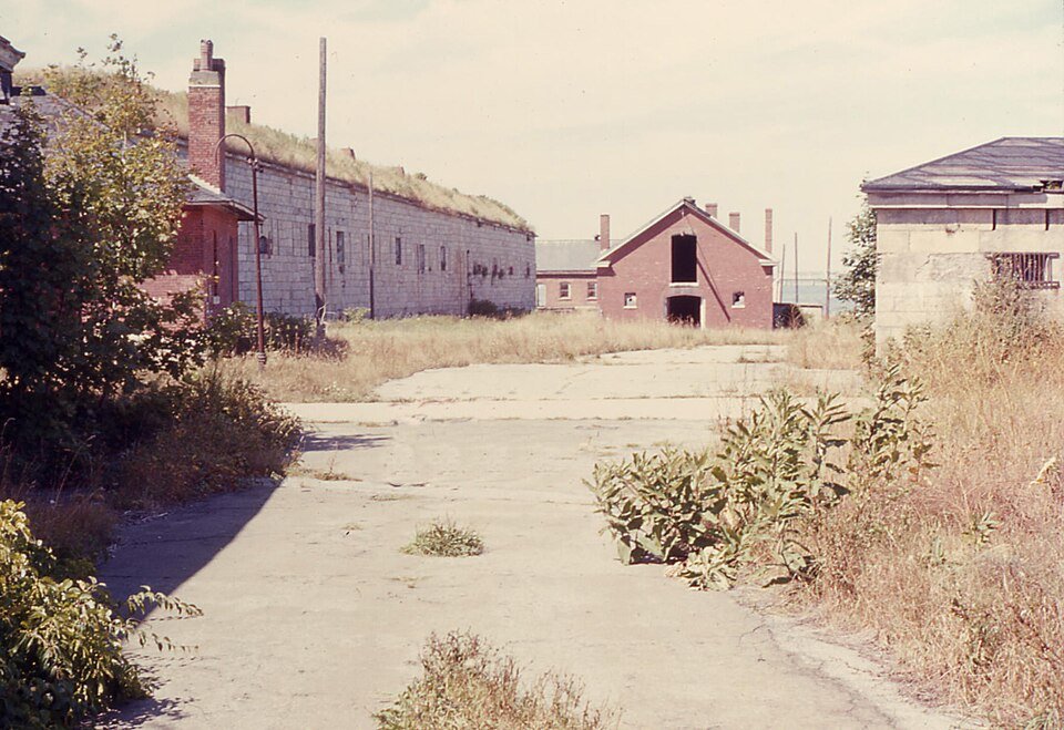 Um pátio tomado pelo mato entre prédios antigos do Fort Adams, em uma fotografia de 1968