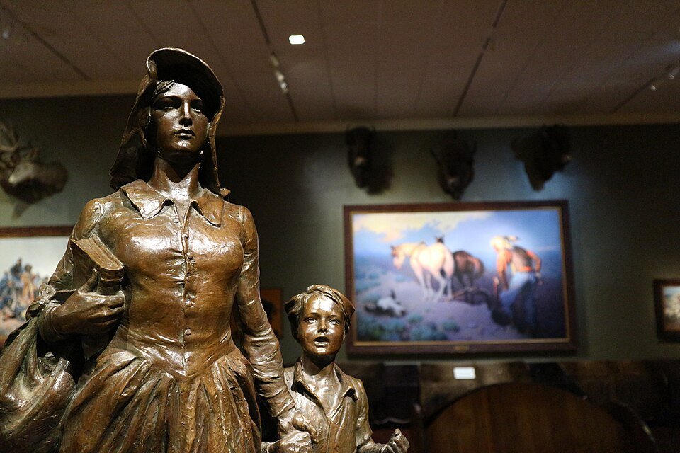 A bronze pioneer woman and child in a gallery of the Woolaroc Museum, with Western paintings behind