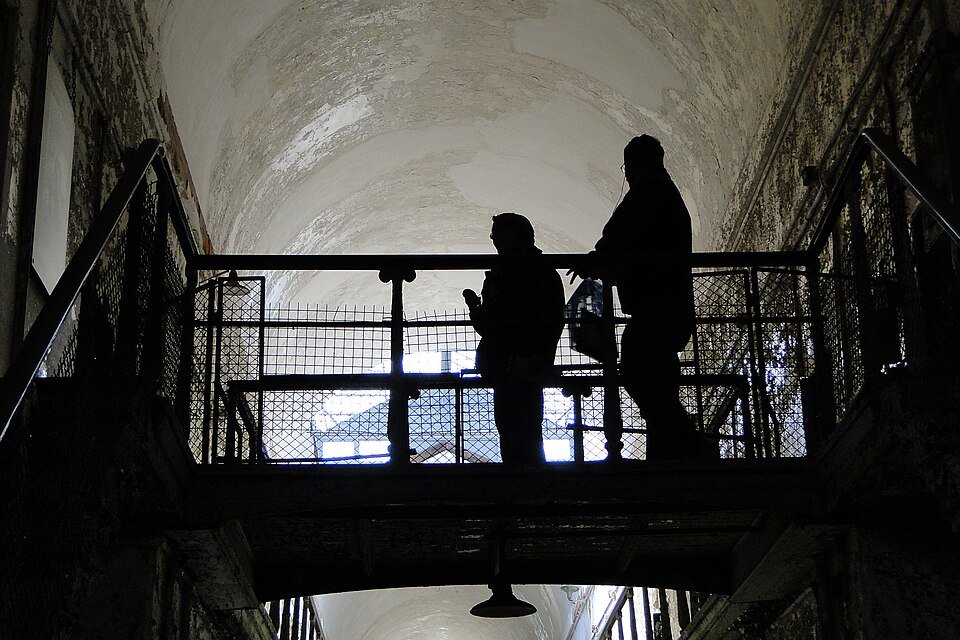 Visitors in silhouette on a walkway in a vaulted corridor at Eastern State Penitentiary